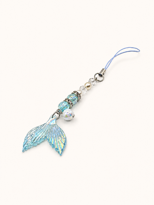 A light blue mermaid tail charm with iridescent glitter, silver beads, and a small pearl bead on a light blue cord, shown on a plain off-white background.